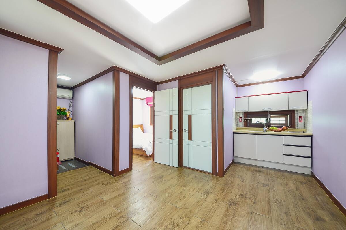 A hallway with wooden flooring, a kitchen with white cabinets, and a ceiling with wooden trim.