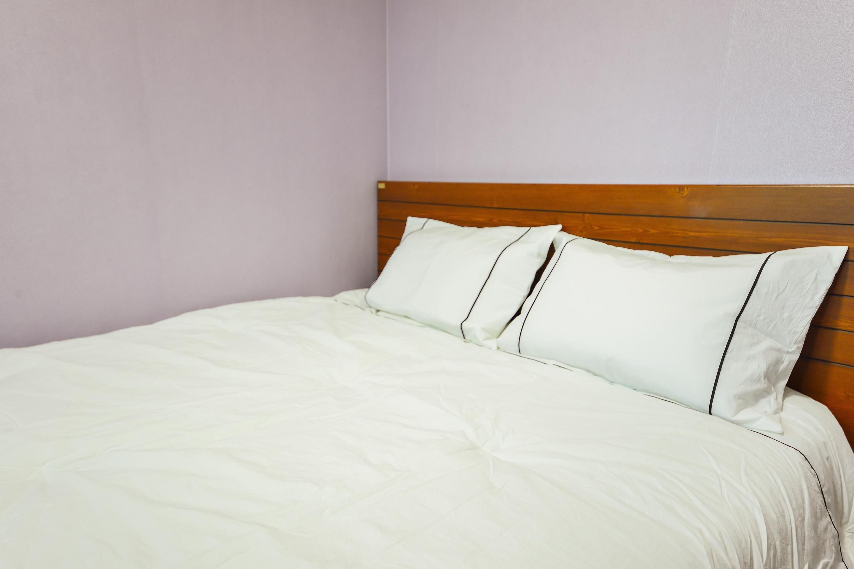 Un lit simple avec une tête de lit en bois et une literie blanche, dans une pièce aux murs de couleur claire.