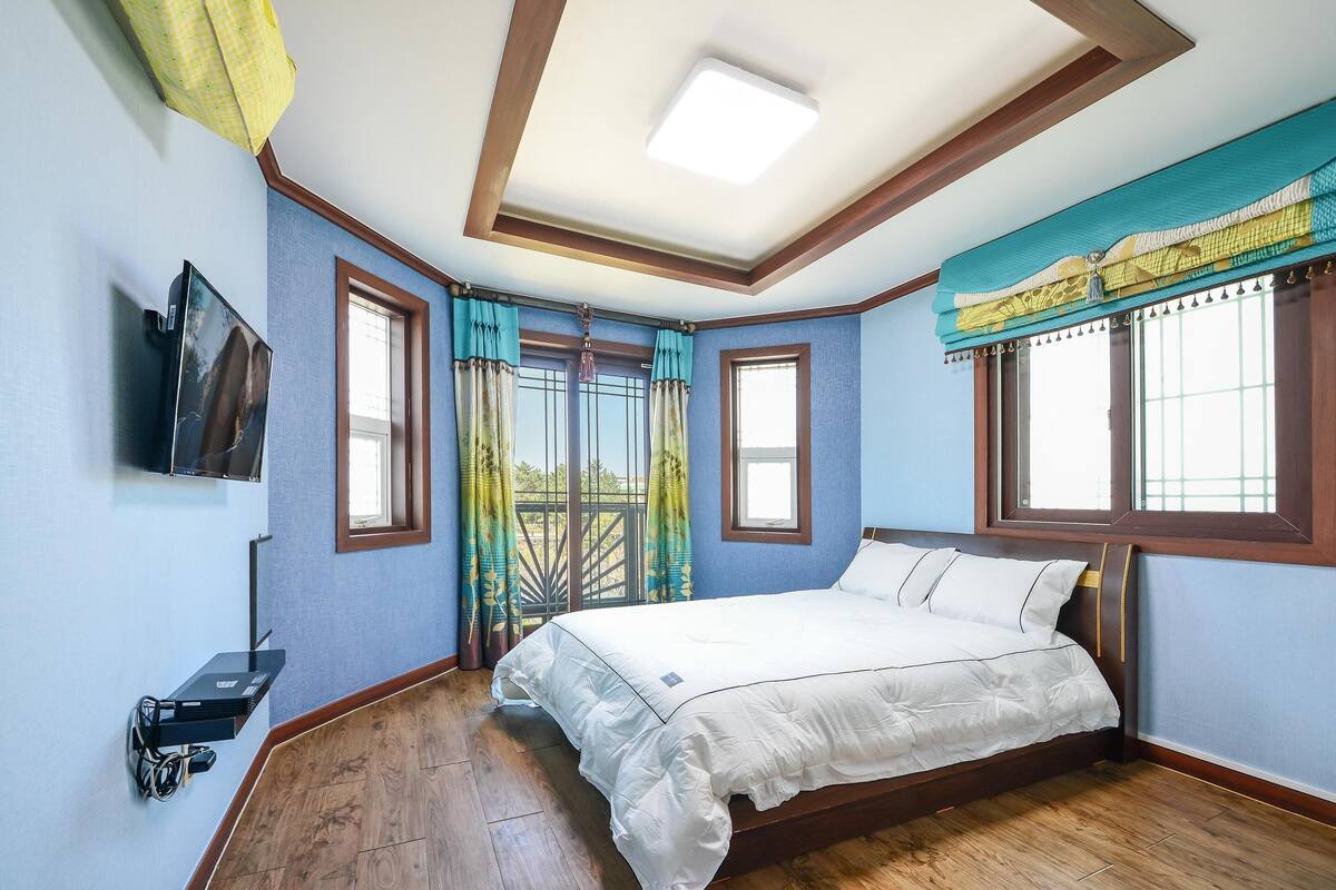 A bedroom with a bed, a TV mounted on the wall, and a window with curtains.