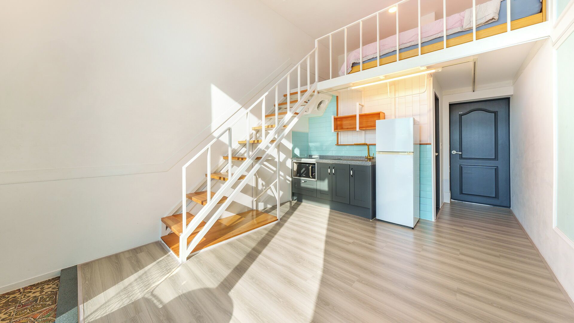 A modern interior with a staircase leading to a loft bedroom, a kitchen area, and a door.