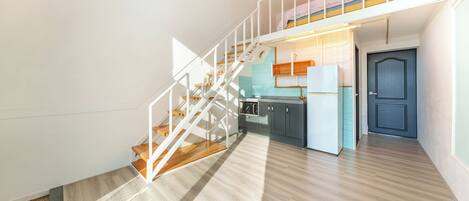 A modern interior with a staircase leading to a loft bedroom, a kitchen area, and a door.