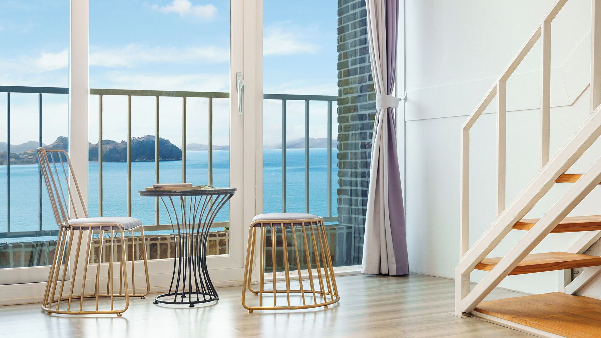 Un balcón con vista al mar, una mesa, dos sillas y una escalera.