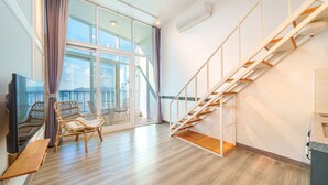 A modern living room with a wooden staircase, a balcony with a view, and wicker furniture. - Yeosu Jplus Pension (Yeosu)