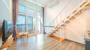 A modern living room with a wooden staircase, a balcony with a view, and wicker furniture. - Yeosu Jplus Pension (Yeosu)