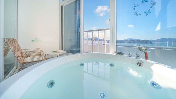 A balcony with a hot tub, a wicker chair, and a table with a plant. - Yeosu Jplus Pension (Yeosu)