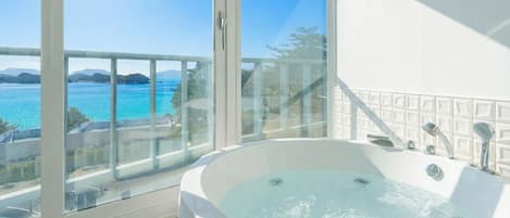 Un baño moderno con una bañera grande, una zona de ducha con mampara de vidrio y vista al mar.