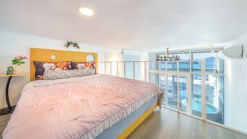 A bedroom with a large bed, a headboard with a mirror, a small table with a vase, and a view of a balcony with a pool.