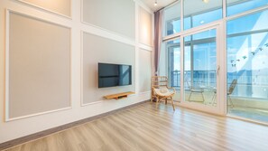 Una habitación moderna con una televisión de pantalla plana en la pared, una silla de mimbre y un gran ventanal de vidrio que da a un balcón exterior con vistas al cielo y a las montañas.
