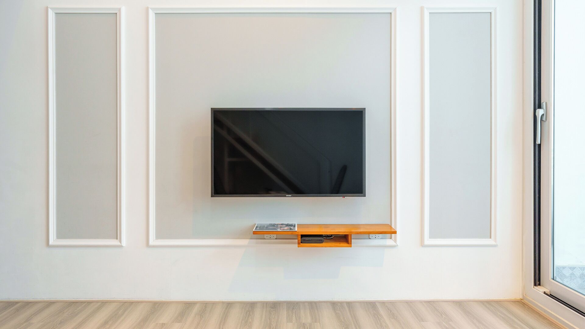 A modern living room with a flat-screen TV mounted on a white wall, a wooden entertainment unit below, and a wooden floor.