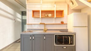 Una cocina moderna con armarios grises, un lavamanos de acero inoxidable, un microondas integrado y estantes de madera sobre la encimera.