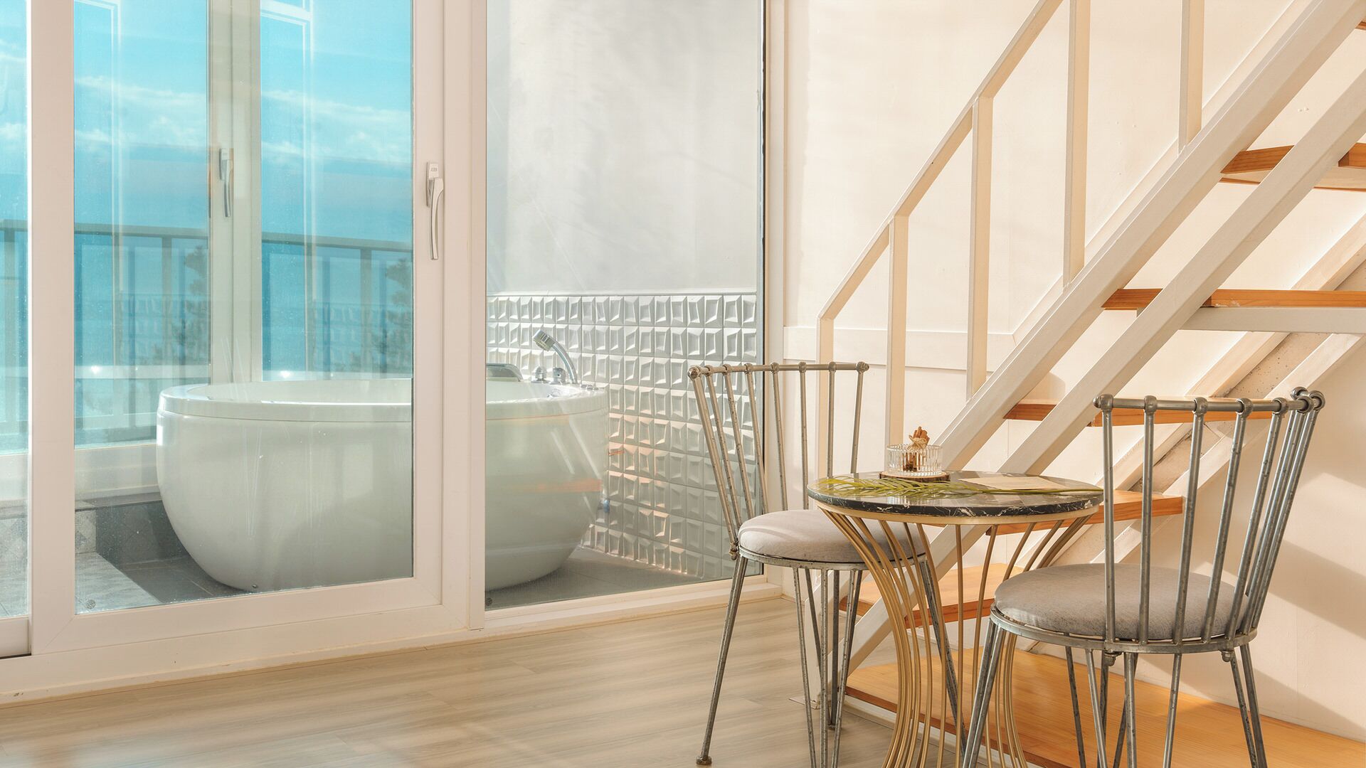 A balcony with a white toilet and a bathtub, a round table with chairs, and a staircase with wooden steps.