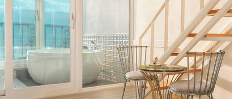 A balcony with a white toilet and a bathtub, a round table with chairs, and a staircase with wooden steps.