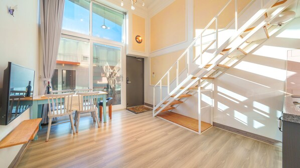 Un espacio habitable amplio con piso de madera, una mesa de comedor con sillas, una escalera y ventanas grandes que dejan entrar luz natural.