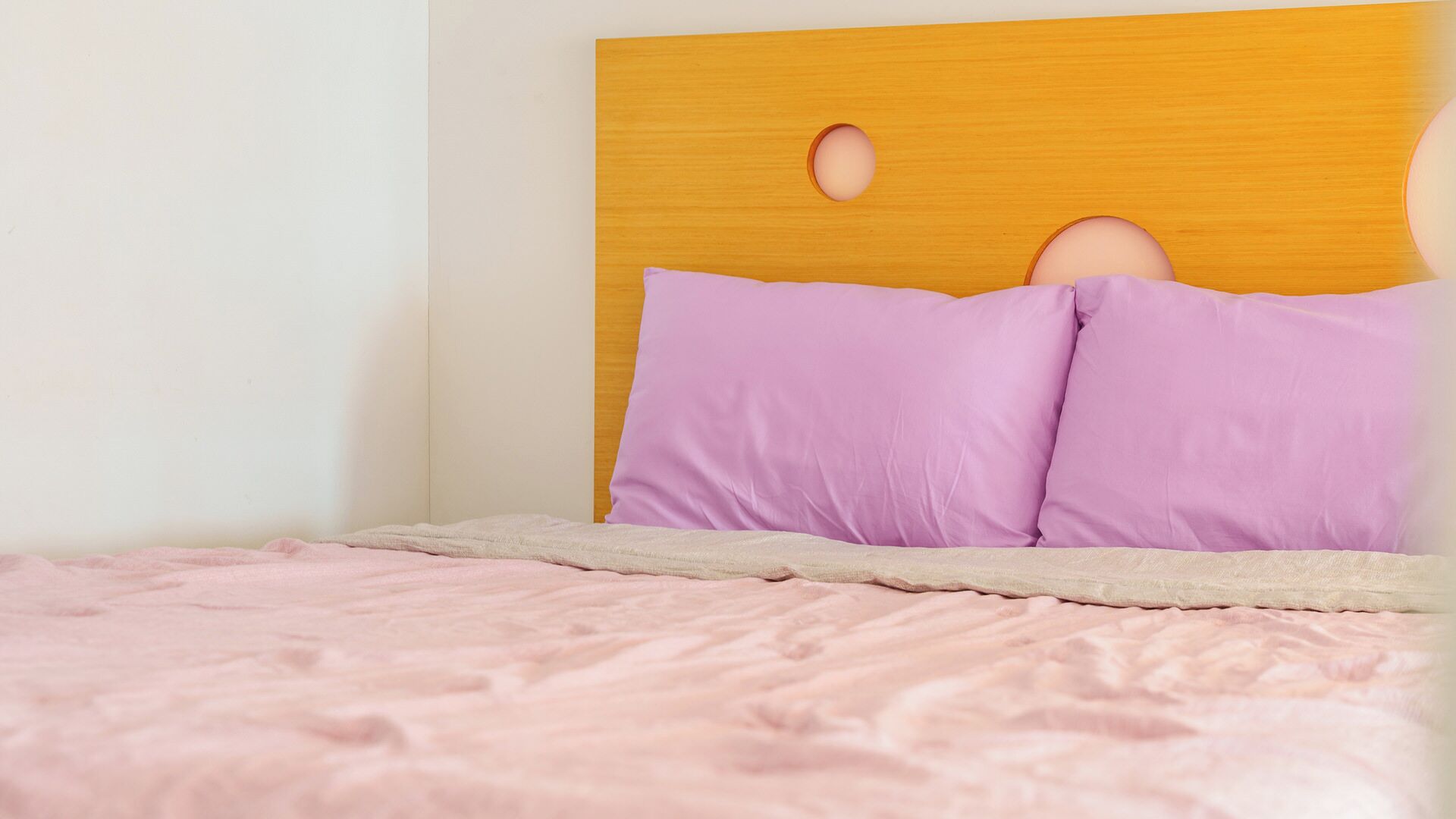 A bed with a wooden headboard, two pillows, and a pink blanket.