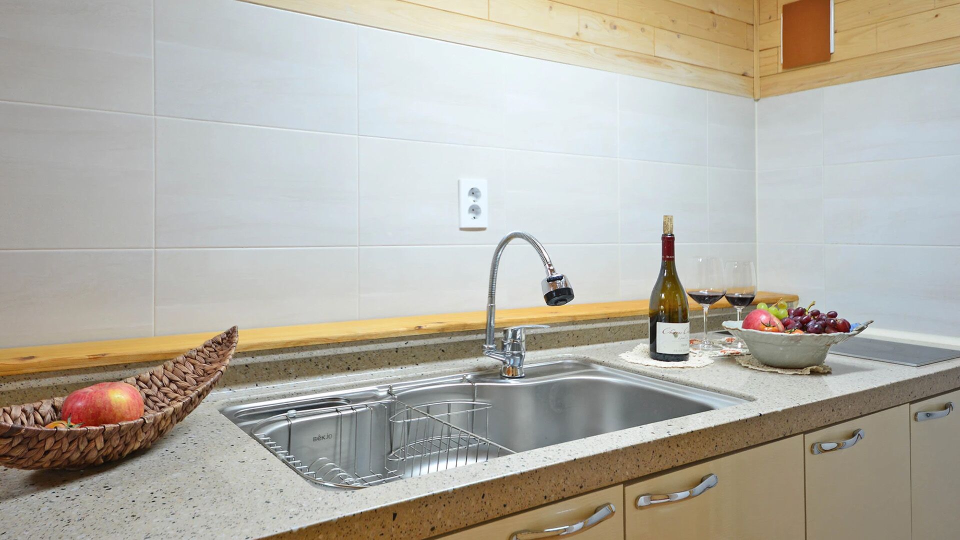 A kitchen with a stainless steel sink, a wine bottle, and a bowl of fruit.