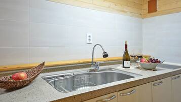 A kitchen with a stainless steel sink, a wine bottle, and a bowl of fruit.