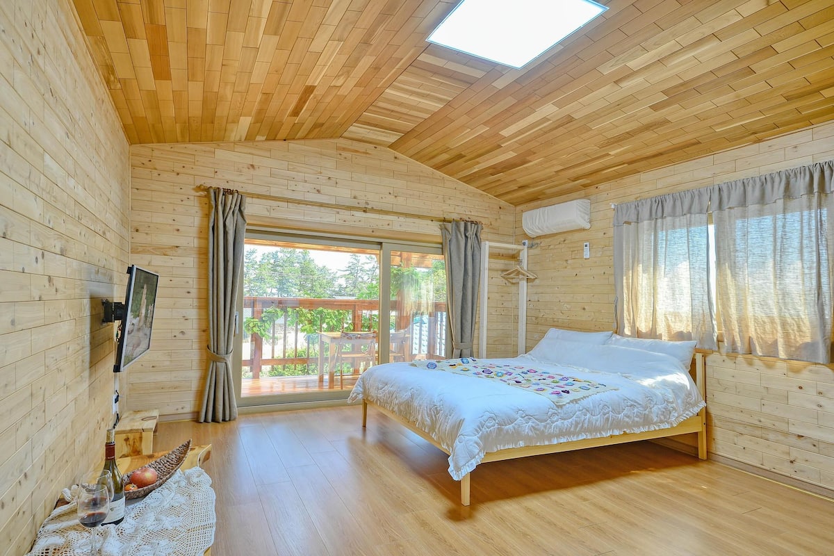 A wooden cabin room with a bed, a TV, and a table with drinks and fruit.