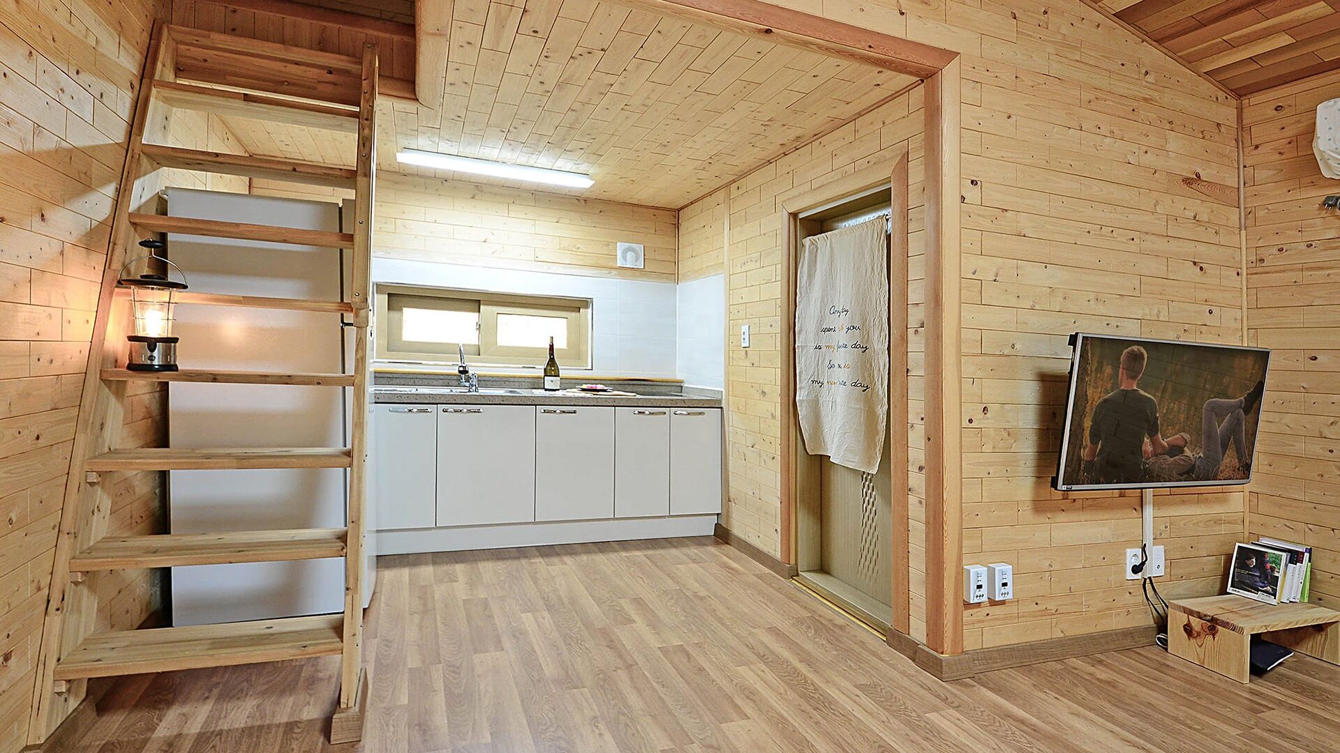 A wooden interior with a kitchen, a ladder, a painting, and a television.