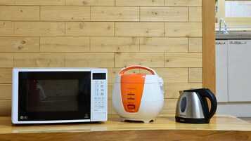 A kitchen with a microwave, a rice cooker, and a kettle on a wooden countertop.