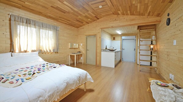 Una cabaña de madera con una cama grande, una zona de cocina y una puerta que da a otra habitación.