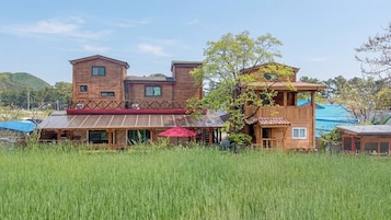 A multi-story wooden building with a flat roof, surrounded by tall grass and trees.
