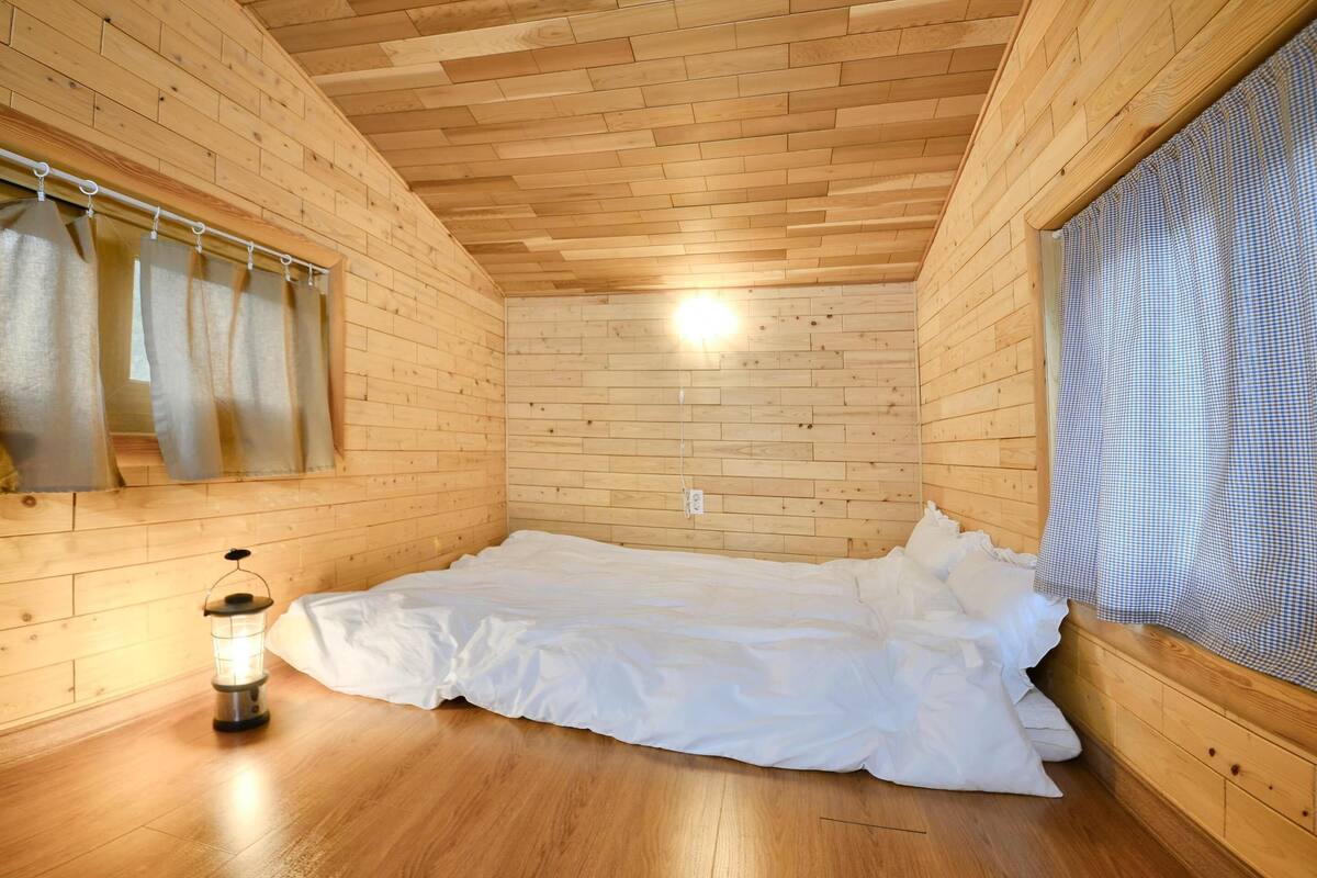 A wooden cabin room with a bed, a lantern, and a window with curtains.