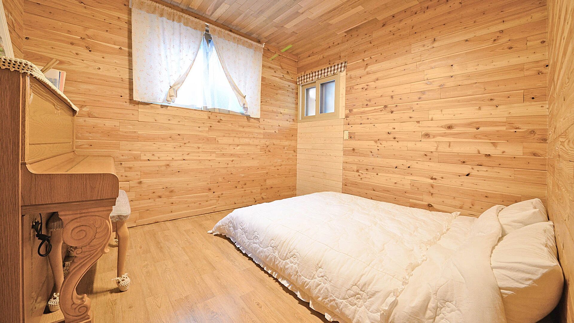 Un dormitorio con paneles de madera, una cama, un aparador y un ventanal con cortinas.