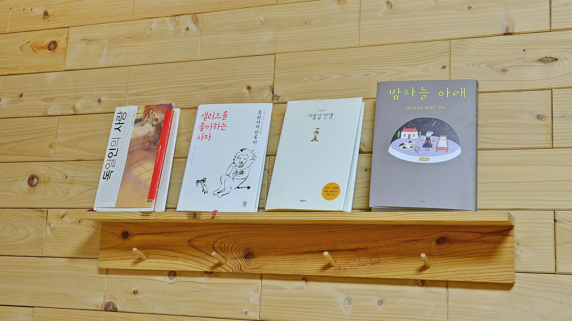 Quatre livres sont posés sur une étagère en bois, adossée à un mur en bois.