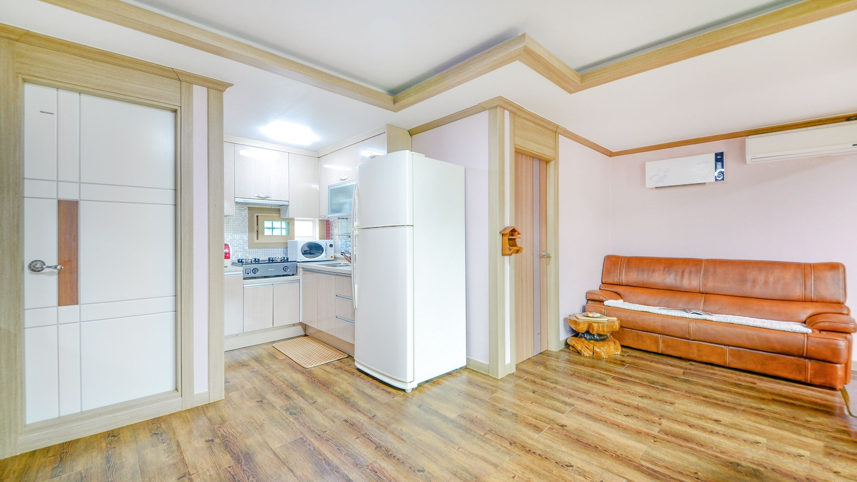 A compact kitchen with a refrigerator, microwave, and stove, adjacent to a living area with a brown leather sofa and a small decorative item.