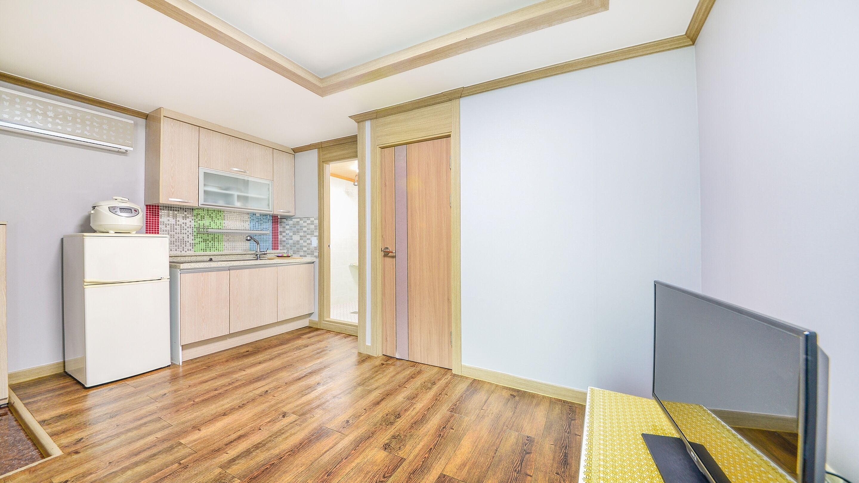 A compact kitchen with wooden flooring, a refrigerator, a microwave, and a tiled backsplash.