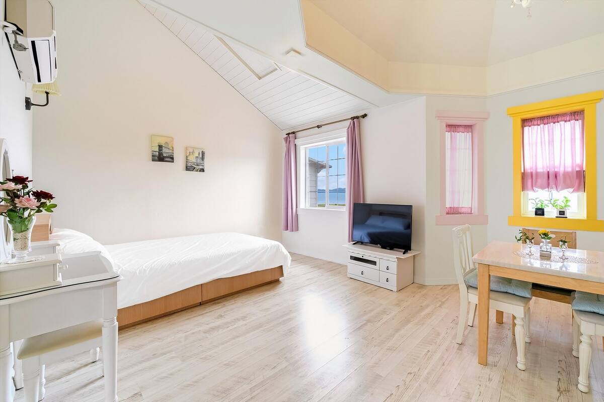 A bedroom with a bed, a TV, a desk, and a window with curtains.