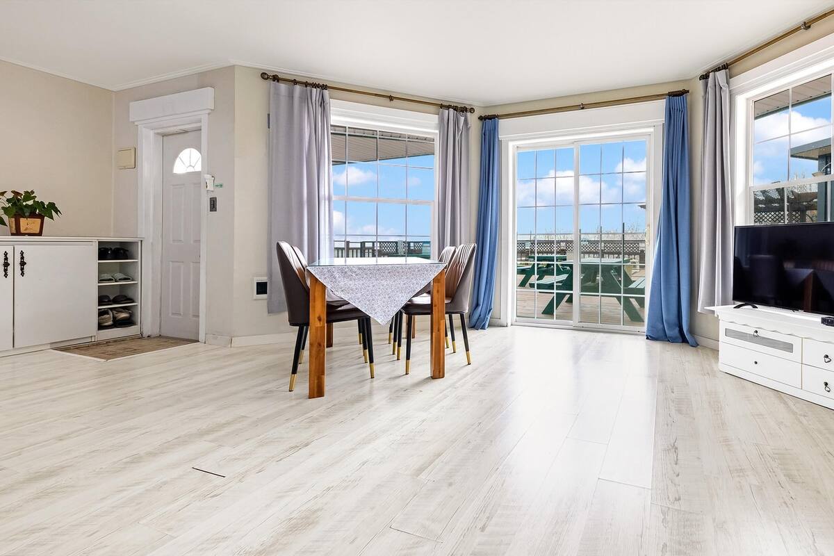 A spacious living room with a dining area, large windows, and a TV.