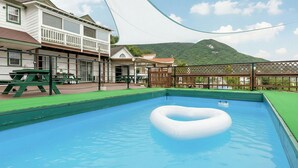 A swimming pool with a floating ring, surrounded by a wooden deck and a green lawn. - Ganghwa Daeun Pension (Incheon)