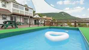 Une piscine avec un flotteur circulaire, entourée d’une terrasse en bois et d’une pelouse verdoyante.