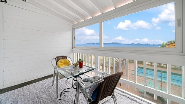 Un balcon avec une table en verre, des chaises en osier et une vue sur la mer.
