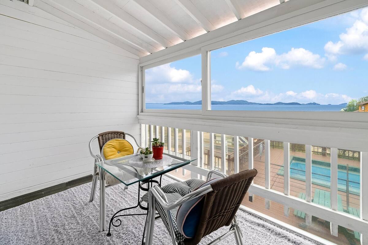 A balcony with a glass table, wicker chairs, and a view of the sea.