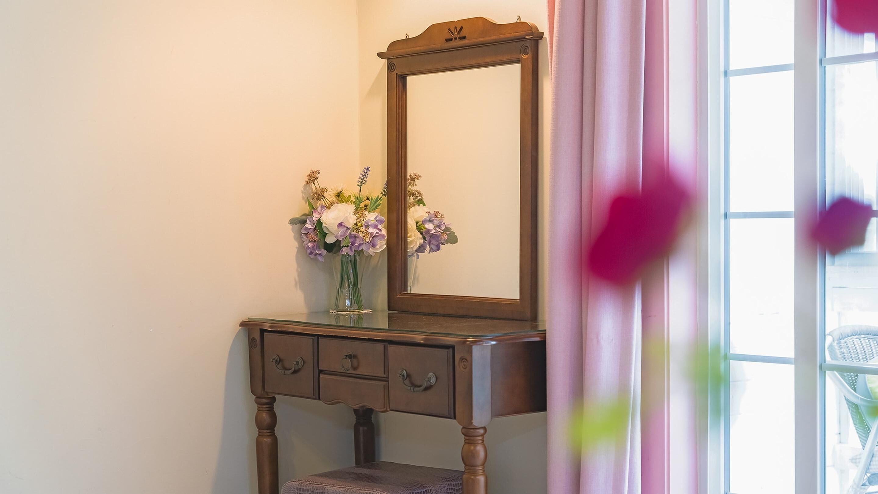 Een houten dressoir met spiegel, een vaas met bloemen en een raam met gordijnen.