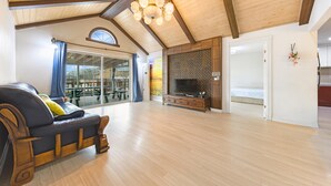 Un salon spacieux avec un plafond en bois, une grande fenêtre, un canapé, un téléviseur et un meuble en bois.