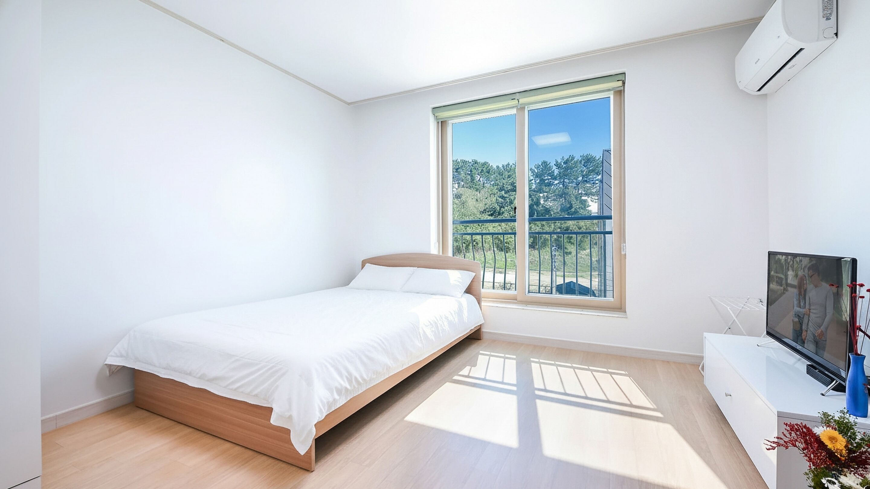 A bedroom with a bed, a TV, and a window with a view of trees.