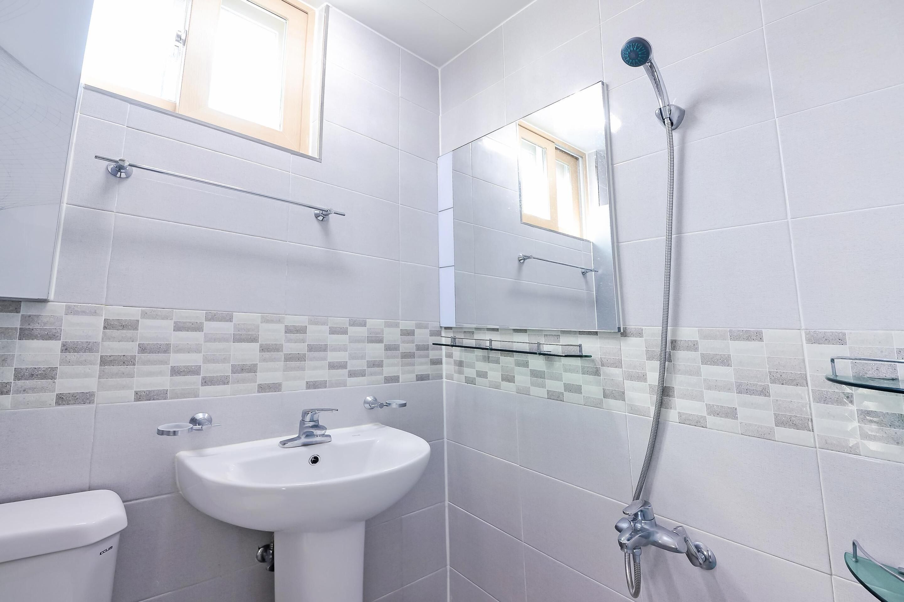 Ein Badezimmer mit Waschbecken, Toilette, Dusche und Handbrause sowie einem Spiegel über dem Waschbecken.