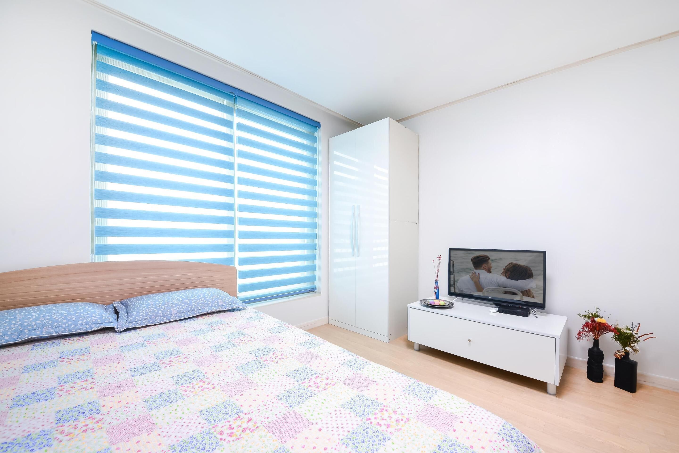 Una camera da letto con un letto, una TV su una cassettiera bianca e una finestra con persiane.
