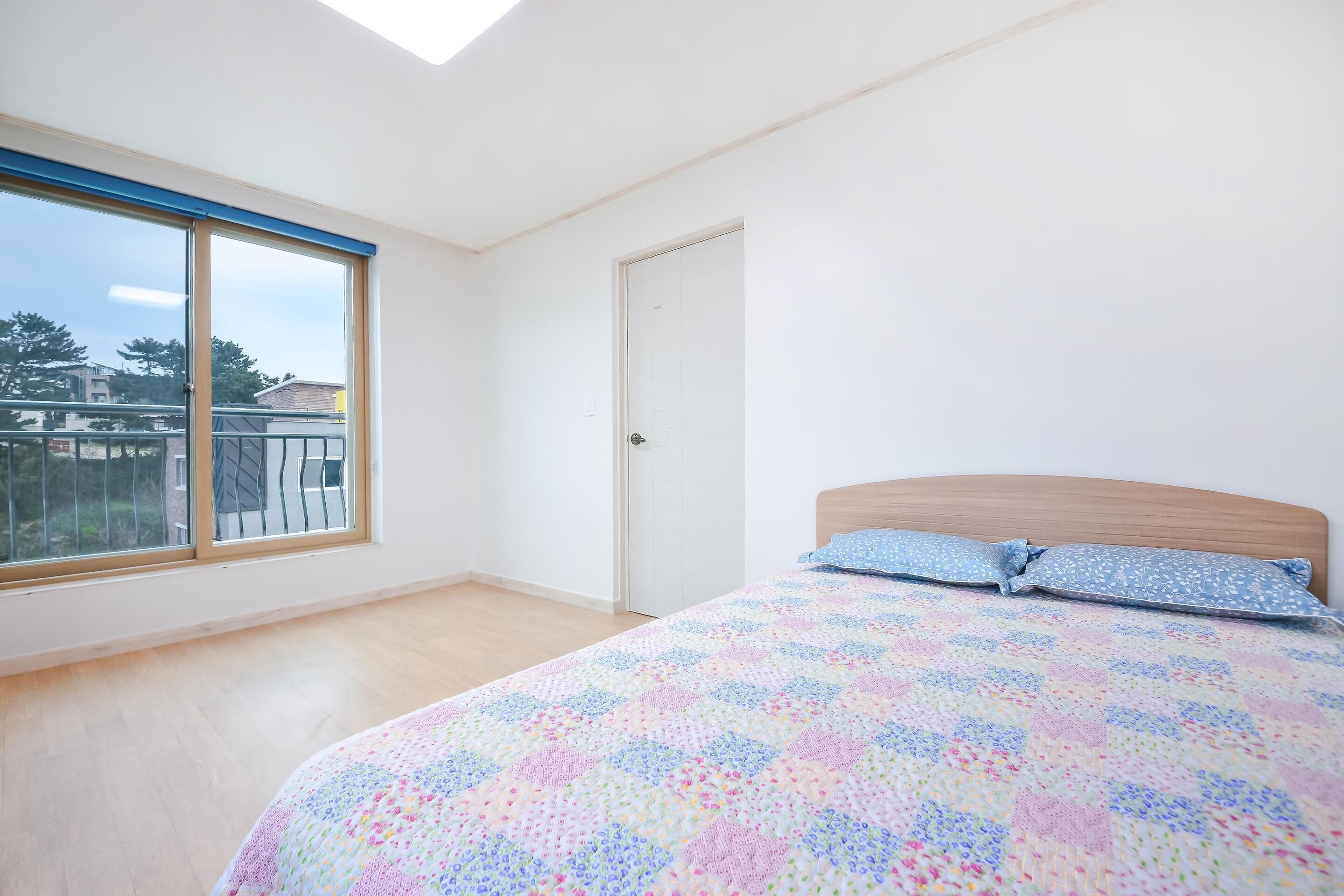 Un dormitorio con un gran ventanal, una cama con colcha estampada y un cabecero de madera.
