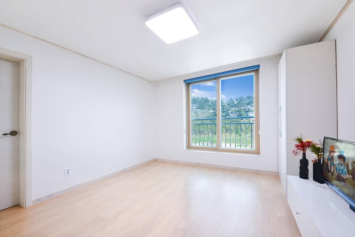 A spacious room with a large window, a flat-screen TV, and a white cabinet.