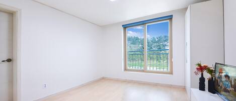 Una habitación amplia con un ventanal grande, un televisor de pantalla plana y un armario blanco.