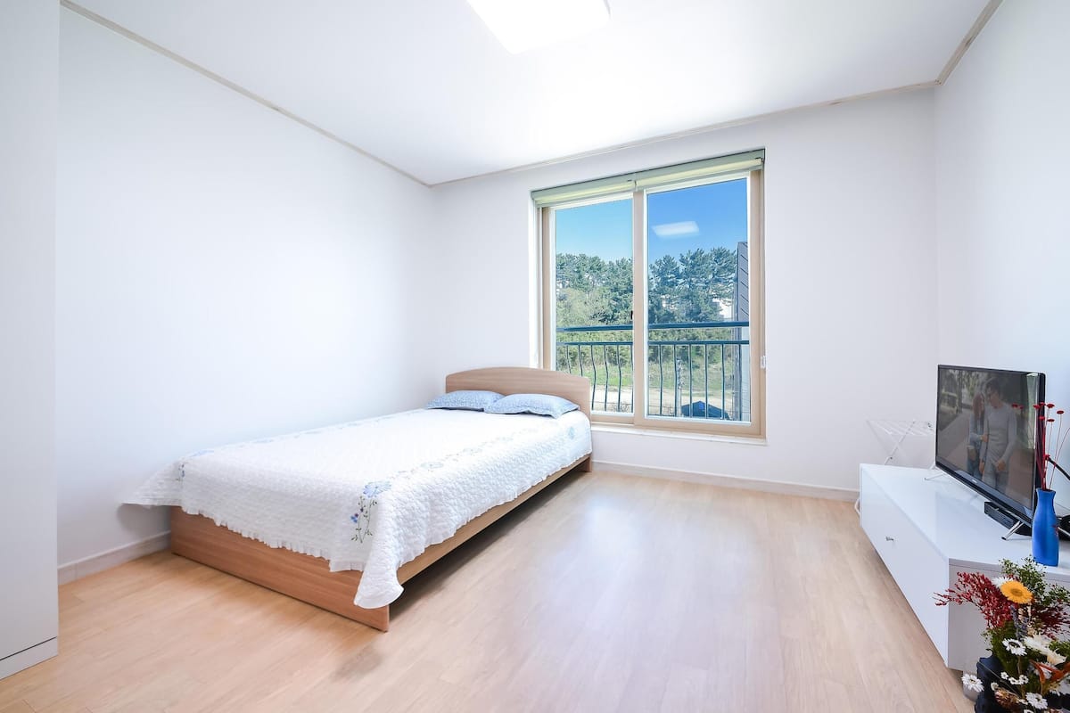 A bedroom with a bed, a TV, and a window with a view of trees.