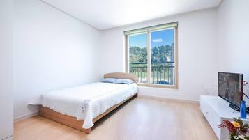 Ein Schlafzimmer mit Bett, Fernseher und Fenster mit Blick auf Bäume.