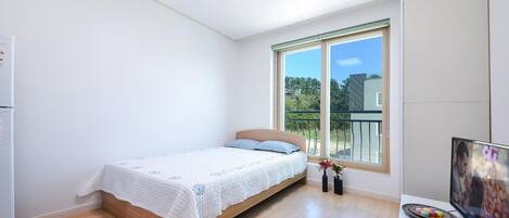A bedroom with a bed, a TV, and a window with a view of greenery.
