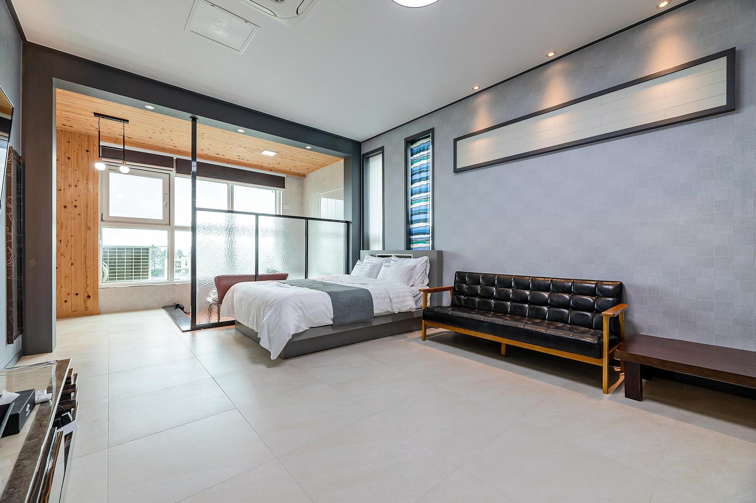 Un dormitorio moderno con cama, un banco y un ventanal grande.