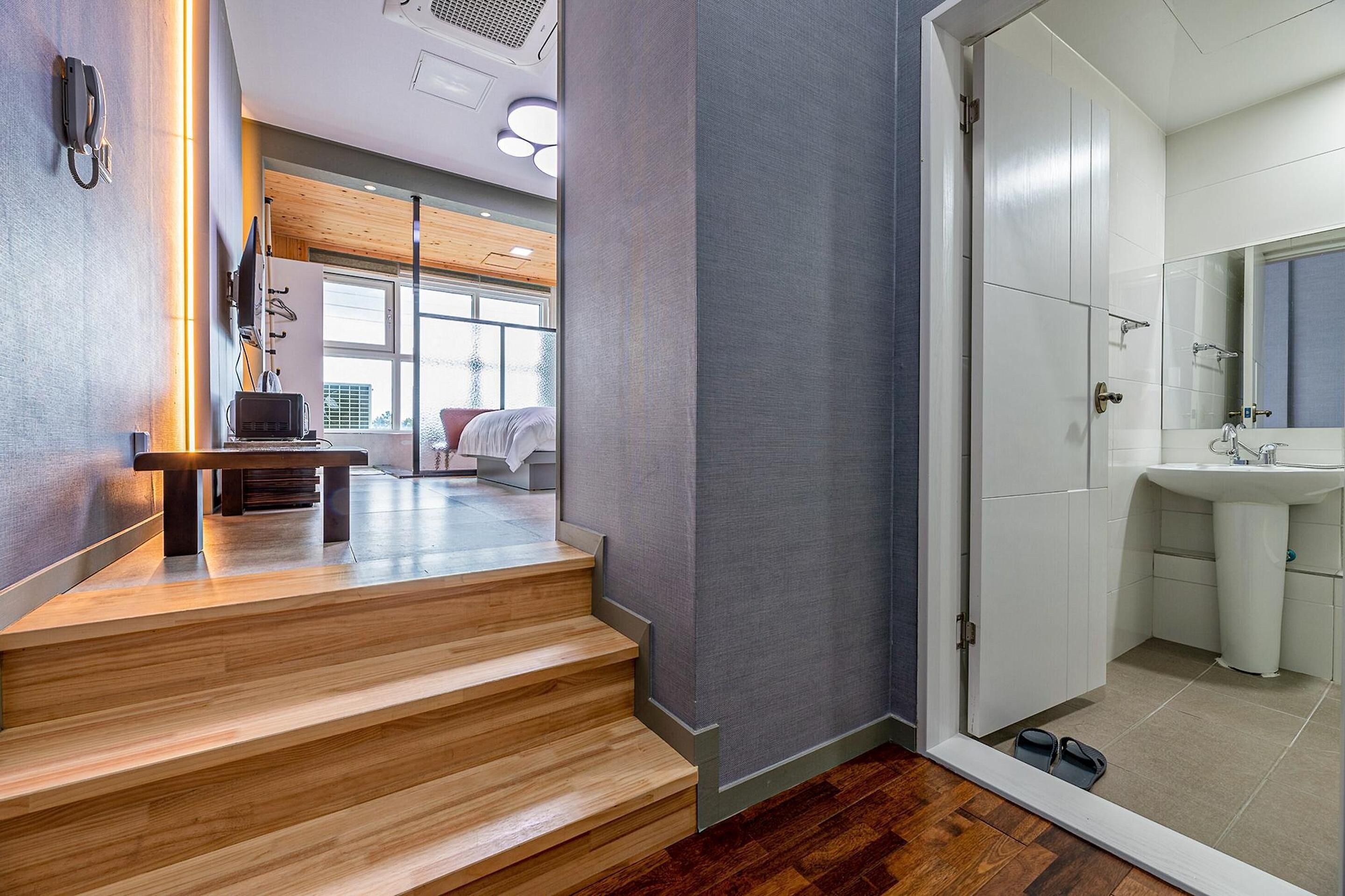 A modern hotel room with a wooden staircase, a large window, and a bathroom with a sink and mirror.