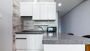 A modern kitchen with white cabinets, a granite countertop, a built-in microwave, and a stainless steel faucet. - Buan Tomynspa Pension (Buan)